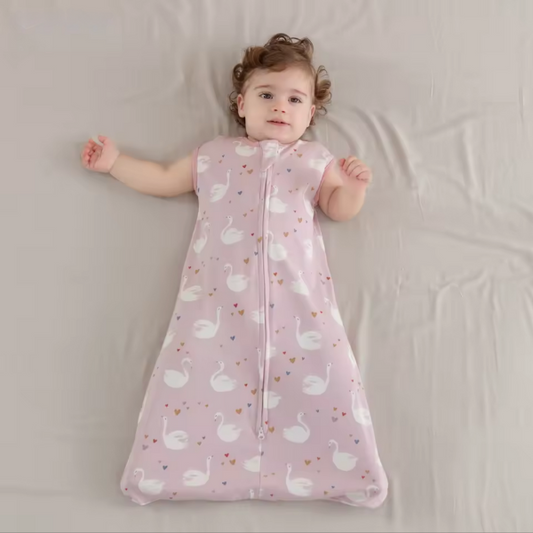 Child wearing a pink swaddle with white swan pattern on a light gray background